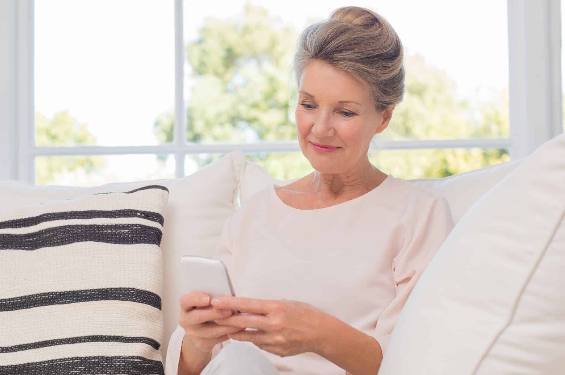 A middle aged woman sits inside her home and uses her cellphone to access the iMist app.